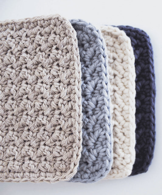 Textured square crochet coasters are lined up, overlapping, focusing on the texture and clean single crochet border.