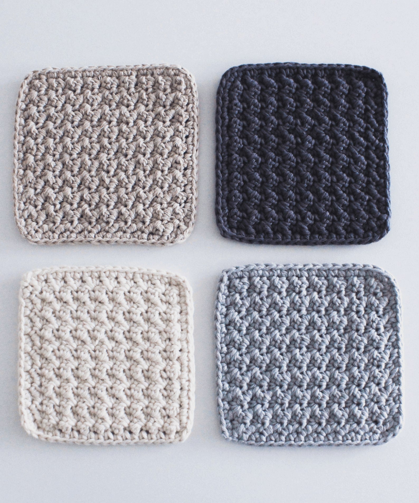 Four textured square crochet coasters in complementary colours are arranged in a neat square.